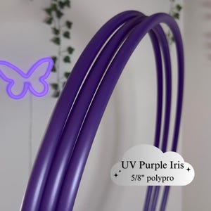 Puede incluir: Primer plano de tres aros de hula-hoop curvos, UV púrpura iris, hechos de tubos de polipropileno de 1,6 cm. Los aros son de un color púrpura vibrante. El texto "UV Purple Iris" y "5/8" polypro" se muestra en un gráfico en forma de nube.