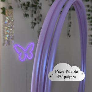 May include: Pixie Purple hula hoop with a 5/8" polypro construction. A neon purple butterfly is in the background. The text "Pixie Purple 5/8" polypro" is on a white cloud-shaped graphic.