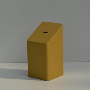 May include: Mustard-yellow, rectangular piggy bank with a slanted top and a slot for inserting money. The bank is made of a solid material and sits on a white surface. The design is minimalist and modern.