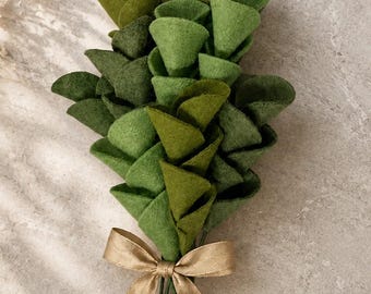 May include: A bouquet of felt flowers in varying shades of green, tied with a gold ribbon. The felt petals are cone-shaped and arranged to resemble a floral arrangement. The stems are green and extend below the ribbon.