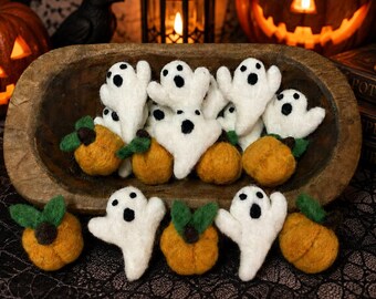 May include: A collection of small, felted wool decorations featuring white ghosts with black eyes and mouths, and orange pumpkins with green leaves. Some are arranged inside a rustic wooden bowl, while others are placed in front of it.