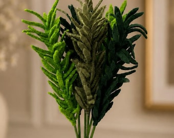 May include: A bouquet of artificial greenery in varying shades of green. The faux plants have a textured, feathery appearance and are arranged in a dark brown vase. The leaves are a mix of light and dark green, creating a natural look for home decor.