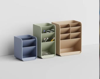 May include: Three desk organizers in blue, sage green, and beige. The blue organizer has two compartments, the green one has three compartments containing pens and scissors, and the beige one has six compartments arranged in a grid-like structure.