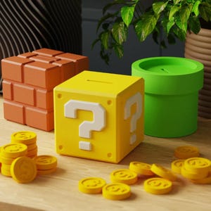 Puede incluir: Un bloque amarillo con un signo de interrogación, un bloque de ladrillos naranja y un recipiente verde con forma de tubería. Monedas amarillas están esparcidas alrededor de los bloques. El bloque de interrogación tiene una ranura en la parte superior. Los objetos están inspirados en un videojuego popular.