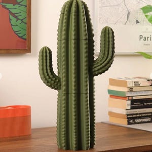 May include: A matte olive green cactus-shaped storage container with a segmented vertical design. The object features a central column with two curved side arms and a ribbed texture throughout, standing upright as a decorative organizational piece.