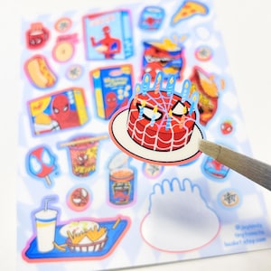 May include: A sticker sheet featuring various food items and character-themed illustrations, including a red and white spider-web patterned birthday cake with blue candles, snack boxes, a hot dog, a drink, and a bowl of noodles on a light background.