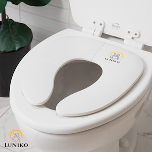 May include: White, foldable toilet seat with a child-friendly design. The seat features a bear and sun logo with the text "LUNIKO". The seat is designed to fit on a standard toilet and is made of durable plastic.