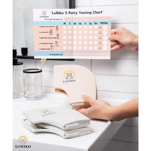 May include: A LuNiko potty training chart with a grid for tracking daily tasks like sitting on the potty, wiping, flushing, and washing hands, alongside two folded, beige, semi-circular plastic stools featuring a bear logo and text.