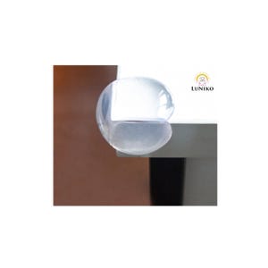 May include: A clear, rounded silicone corner protector attached to the edge of a white table. The protector is transparent and smooth, designed to cover sharp corners. The logo LUNIKO with a small bear icon is visible on the white surface.