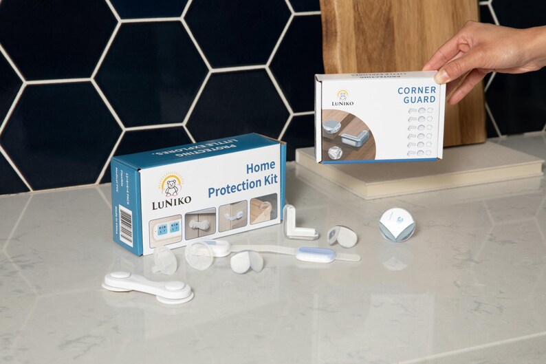 May include: A Luniko Home Protection Kit box and a Corner Guard box, featuring white and blue child safety components including adhesive corner protectors, cabinet locks, and strap locks displayed on a surface with product packaging imagery.