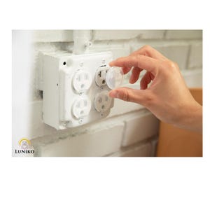 May include: A clear plastic outlet plug cover being inserted into a white four-gang electrical wall receptacle. The receptacle is mounted on a white painted brick wall. The brand name LUNIKO is printed in the bottom left corner of the image.