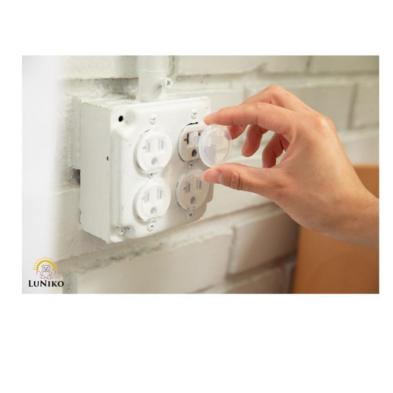 May include: A clear plastic outlet plug cover being inserted into a white four-gang electrical wall receptacle. The receptacle is mounted on a white painted brick wall. The brand name LUNIKO is printed in the bottom left corner of the image.