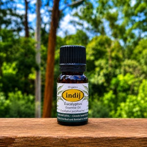 May include: A small amber glass bottle of organic eucalyptus essential oil with a black cap. The white label features the brand name indij, the text Eucalyptus Essential Oil, Eucalyptus polybractea, 100% NATURAL, Cineole level 81.3%.