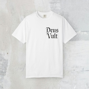 Könnte beinhalten: Ein weißes T-Shirt mit dem Aufdruck "Deus Vult" in schwarzer gotischer Schrift auf der rechten Brust. Das Shirt hat einen Rundhalsausschnitt und kurze Ärmel. Der Stoff scheint eine weiche Baumwollmischung zu sein.