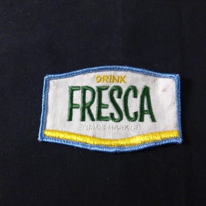Könnte beinhalten: Gestickter Aufnäher mit dem Wort "FRESC" in Grün, "DRINK" darüber und "TRADE MARK" darunter. Der Aufnäher hat einen weißen Hintergrund, einen blauen Rand und einen gelben Streifen unten.
