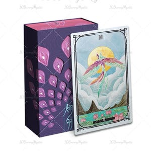 May include: A tarot card deck with a purple box featuring a pattern of pink and purple shapes. The card shows a colorful phoenix against a backdrop of a yellow moon, mountains, and clouds. The text "10 Bunny Mystic" is visible.