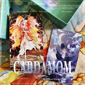May include: Two tarot cards with colorful illustrations. One card features a figure with fiery wings, the other a witch with a wand under a starry sky. The word "CARDAMOM" is printed across the cards.