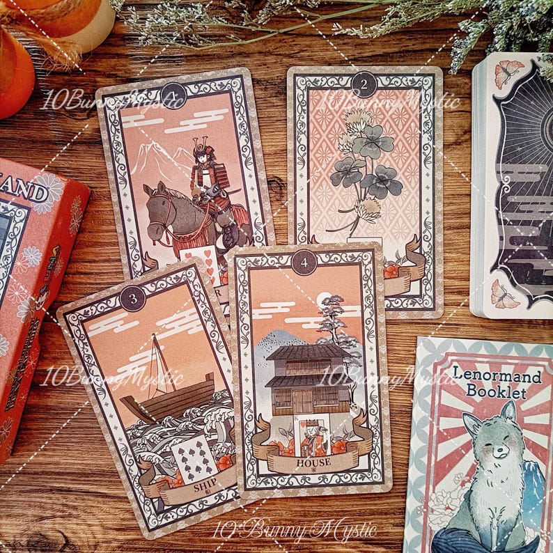 K&ouml;nnte beinhalten: Ein Set Lenormand-Orakelkarten in gedeckten Pfirsich- und Braunt&ouml;nen mit kunstvollen R&auml;ndern. Die Karten zeigen Illustrationen eines Samurai zu Pferd, eines Kleeblatts, eines Schiffes auf Wellen und eines Hauses sowie ein Begleitheft mit einem Fuchs.