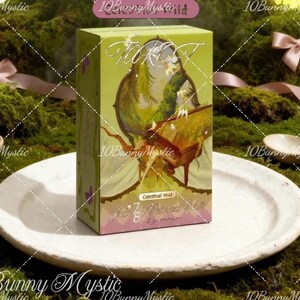 May include: A green and pink tarot card box with the words "Tarot" and "Celestial Wild" visible. The box features an illustration of a figure with a musical instrument. The box is on a white plate.