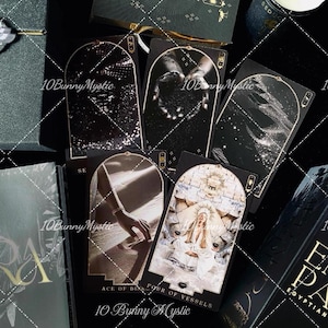 Puede incluir: Una colección de cartas de tarot con imágenes oscuras y atmosféricas que presentan temas celestiales y desérticos. Las cartas muestran bordes dorados intrincados, marcos arqueados y el texto "Ace of Disks" y "Four of Vessels" en la baraja.