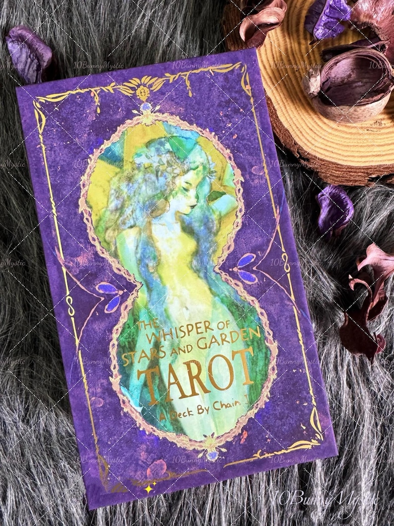 May include: A tarot card deck with a purple cover featuring a watercolor illustration of a woman with long hair. The text "The Whisper of Stars and Garden Tarot" is displayed in gold lettering. The deck is a "Deck By Chain".
