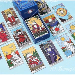 May include: A deck of tarot cards featuring illustrations of dogs in various roles, including The Magician, The Empress, and The High Priestess. The cards are displayed around a blue box with a white fox logo, all set against a light blue background.