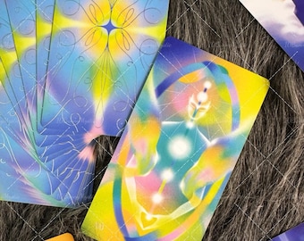 May include: A deck of tarot cards featuring vibrant, multi-colored gradients of yellow, blue, and purple. One card displays a central figure with glowing chakras and the text THE WORLD. Another card shows a figure with an infinity symbol.