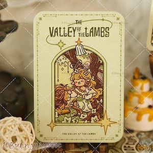 May include: A rectangular, light green tin with the text "THE VALLEY OF THE LAMBS" in a decorative font. The tin features an illustration of a girl with long blonde hair and a lion. The design includes stars and a floral border.