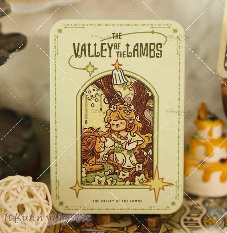 May include: A rectangular, light green tin with the text "THE VALLEY OF THE LAMBS" in a decorative font. The tin features an illustration of a girl with long blonde hair and a lion. The design includes stars and a floral border.