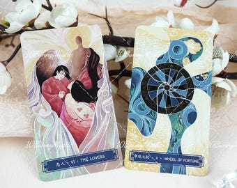 May include: Two rectangular tarot cards featuring artistic illustrations. The left card, labeled VI THE LOVERS, depicts two figures in red and pink robes. The right card, labeled X WHEEL OF FORTUNE, shows a dark blue circular wheel design.