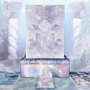 Puede incluir: Un set de caja rectangular titulado The Age of Aquarius Tarot con un diseño etéreo en blanco y azul con delfines y una concha central. La caja se acompaña de una pirámide de cristal transparente y dos cartas de tarot The Fool y The High Priestess.