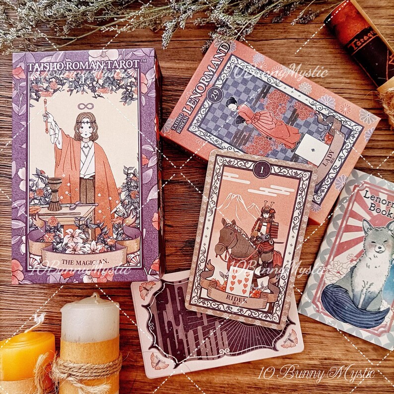 K&ouml;nnte beinhalten: Eine Taisho Roman Tarot-Schachtel mit dem Magier, eine Lenormand-Schachtel mit einer Dame-Karte, eine Reiter-Karte mit einem Samurai auf einem Pferd, ein Lenormand-Buch, eine dunkle Karte mit Schmetterlingen und zwei mit Kordel umwickelte Stumpenkerzen.