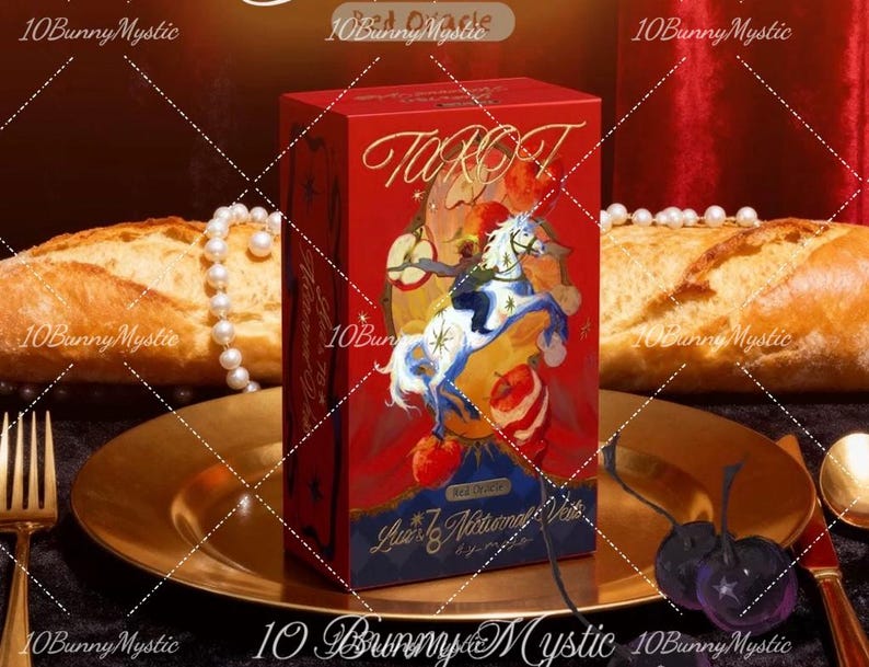 May include: A red tarot card box with gold lettering and a colorful illustration of a horse and rider. The box is on a gold plate with bread, pearls, and cutlery in the background. The text "Tarot" is visible.