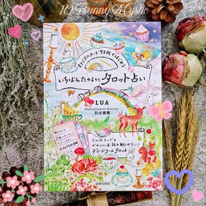 May include: A vibrant tarot card deck, "Day Dream Tarot", with illustrations of cupcakes, animals, and teacups. The cover features Japanese text and the artist's name, LUA. The deck is surrounded by decorative elements.