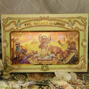 May include: A decorative box with the text "THE VALLEY OF THE LAMBS" features an illustration of an angel and figures in a landscape. The box has a gold and green border with ornate details and a small emblem at the bottom.