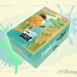 May include: A teal box of the card game "Uno with the Sun" featuring a colorful illustration of a person with a backpack. The box has the game title in white and black text. Splashes of green and blue surround the box.