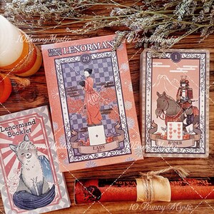 K&ouml;nnte beinhalten: Ein Taisho Roman Lenormand-Kartendeck mit einer Dame-Karte mit einer Frau im roten Kleid, einer Reiter-Karte mit einem Samurai zu Pferd und einem Lenormand-Begleitheft mit Fuchs-Illustration. Die Karten haben verzierte R&auml;nder.