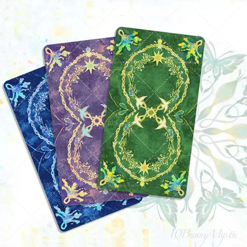 May include: Three tarot cards with ornate designs. The cards are in shades of blue, purple, and green. Each card features a central design of a star and floral elements. The corners of the cards have decorative floral accents. The cards are arranged at an angle.