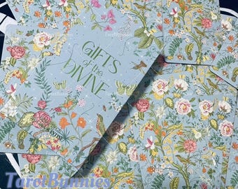 May include: A deck of cards with a floral design and the text "GIFTS of the DIVINE". The cards have a light blue background with illustrations of flowers, birds, and butterflies. The overall theme is spiritual and nature-inspired.