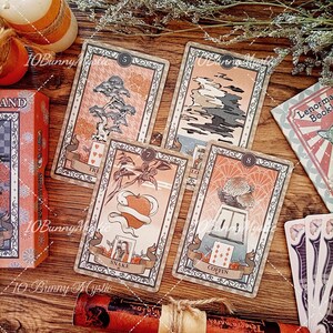 K&ouml;nnte beinhalten: Ein Lenormand-Orakelkartendeck mit vier rechteckigen Karten, die mit den Nummern 5, 6, 7 und 8 versehen sind. Die Karten zeigen Illustrationen eines Baumes, Wolken, einer Schlange um einen Apfel und eines Sarges mit Blumen sowie eine Schachtel.