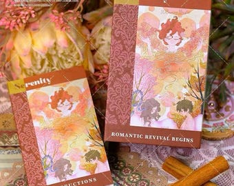 May include: Two decorative boxes with the word "Serenity" on the cover. The boxes have illustrations of figures in a dreamlike setting. The text "Romantic Revival Begins" and "Instructions" are also visible. Cinnamon sticks are in the foreground.