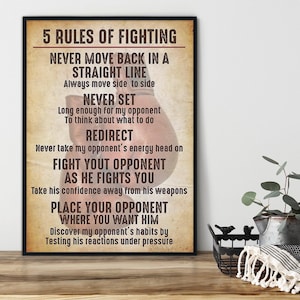 May include: A framed print with the text "5 Rules of Fighting" in a bold font. The text is in a black font on a tan background. The print is in a black frame and is displayed on a wooden surface.