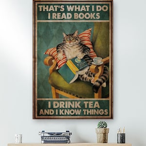 May include: A framed poster featuring a tabby cat seated in a vintage armchair, reading a book and holding a teacup. The poster has text that reads "THAT'S WHAT I DO I READ BOOKS I DRINK TEA AND I KNOW THINGS."