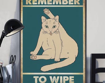 Peut inclure: Une affiche encadrée représentant un chat beige dans une pose humoristique, se léchant l'arrière-train. Le chat est placé sur un fond bleu sarcelle avec les mots "REMEMBER" et "TO WIPE" en lettres dorées.