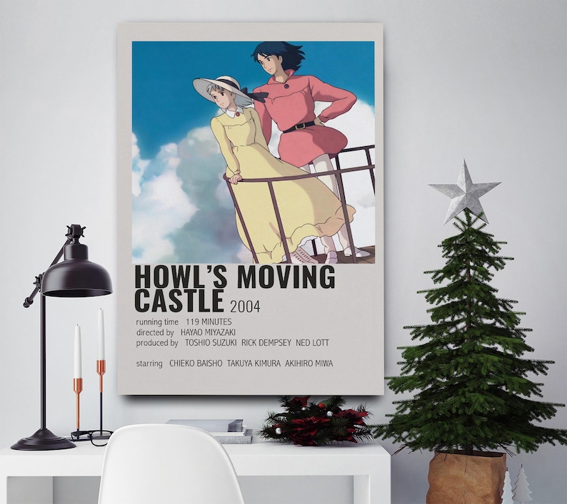 May include: A framed poster for the animated film "Howl's Moving Castle" with two characters on a balcony against a cloudy sky. The poster includes the film's title, year, and credits. A Christmas tree and desk lamp are in the foreground.