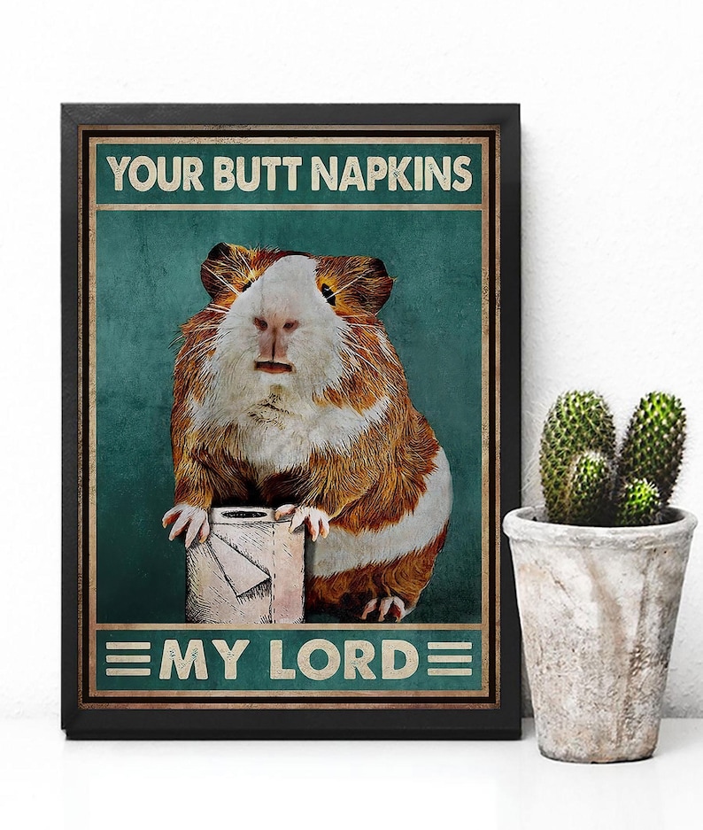 May include: Framed poster featuring a guinea pig holding a roll of toilet paper. The poster has the text "YOUR BUTT NAPKINS" above the guinea pig and "MY LORD" below. The background is teal with a distressed texture.