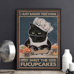May include: Framed poster featuring a black cat wearing a chef's hat with a skull, apron, and baking cupcakes. Text reads "I JUST BAKED YOU SOME" and "SHUT THE FUCUPCAKES."
