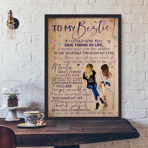 Puede incluir: Una impresión enmarcada con un fondo de madera presenta el texto "To My Bestie" y un mensaje sincero. Dos mujeres ilustradas están sentadas en un banco. La impresión se exhibe sobre una mesa de madera con una lámpara decorativa y una vitrina de cristal.
