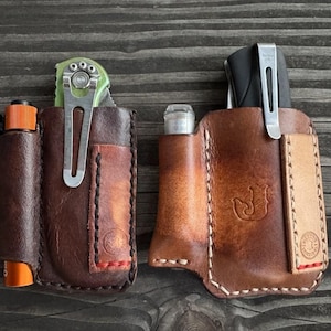 May include: Two brown leather EDC (Every Day Carry) organizers. One holds a knife and an orange flashlight, the other holds a pen and a small vape. Both have metal clips and decorative stitching.