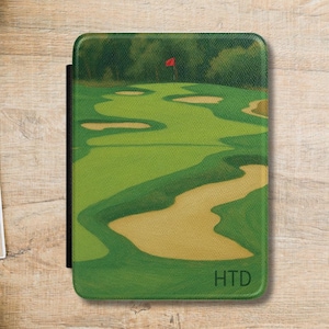 May include: A green golf course design on a tablet case with a red flag, sand traps, and the initials HTD. The case is on a wooden surface with a notepad, pen, coffee cup, and a plant.